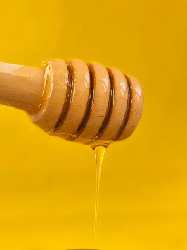 Un hilo de miel cayendo de una cucharilla de madera sobre un fondo amarillo