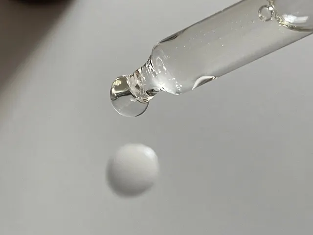 Un cuentagotas de cristal con líquido transparente soltando una gota redonda sobre una superficie gris