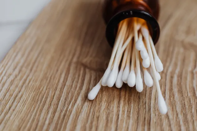 Bastoncillos de algodón asomando de un frasco ámbar sobre una mesa de madera clara