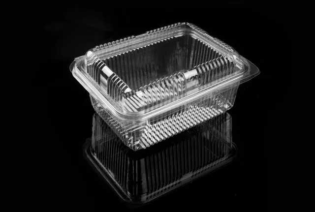 Tarrina de plástico transparente con tapa abatible sobre un fondo negro brillante